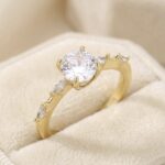 Inel placat cu aur 14K, model elegant cu piatră centrală rotundă și cristale laterale, mărimea 7, Noem®