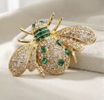 Broșă placată cu aur de 14K, model albină cu pavaj de cristale clare și inserții verde smarald, Noem®