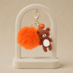 Breloc simpatic cu ursuleț maro, pompon pufos portocaliu și clopoțel, lungime 13 cm, Noem®